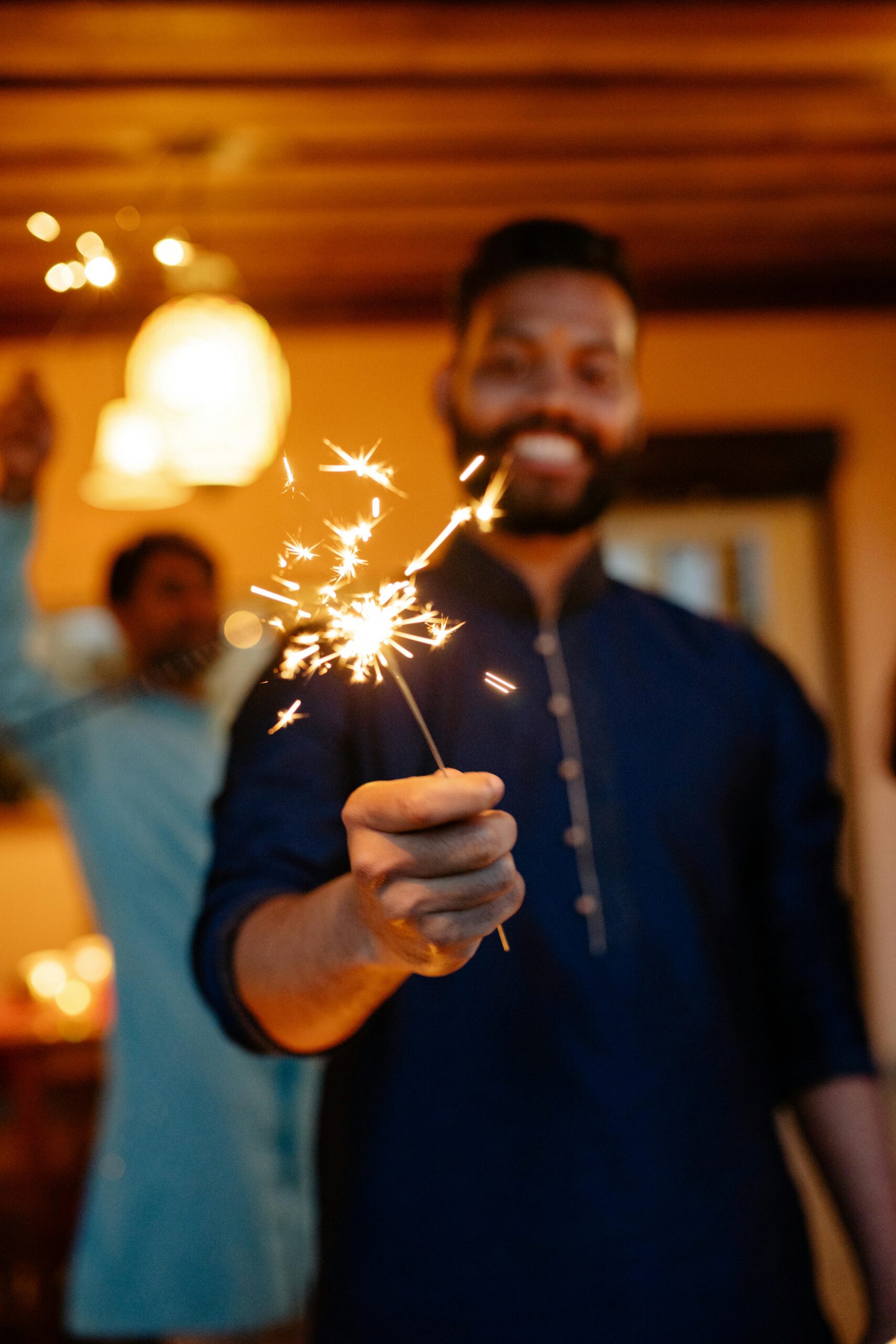 Close-up of a man holding a bright sparkler during a festive indoor celebration, creating a warm and joyful atmosphere.